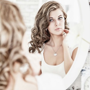 A young woman looks at herself, critically, in the mirror.