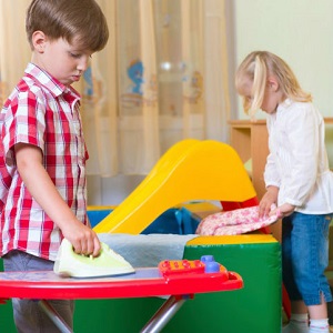 A boy plays with a toy ironing board and a girl plays with folding clothes. 