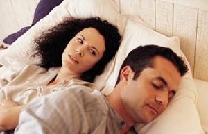 Unhappy woman and sleeping man lying in bed