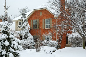 A Victorian looking red-brick house is nestled in snow and trees.