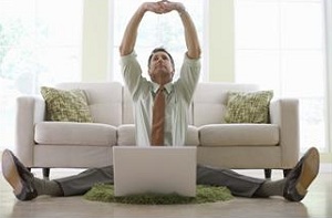 Man sitting on floor in front of couch and stretching with laptop