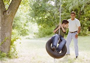 A man pushes his son on a tire swing.