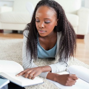 A young woman lies on the floor, studying with books and a notebook.