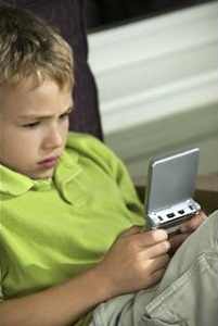 A boy sits in a chair playing a Gameboy with total concentration showing on his face.