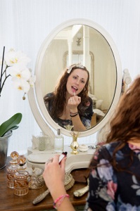 A girl applies lipstick in mirror.