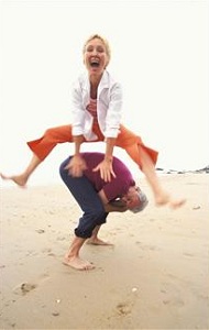 Woman jumping over man on beach