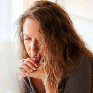 A woman rests her chin on her hands, looking sad and deep in thought.