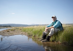 A contemplative fisher sits on bank.
