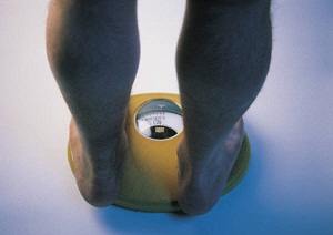 A person's lower legs and feet are shown standing on a scale.