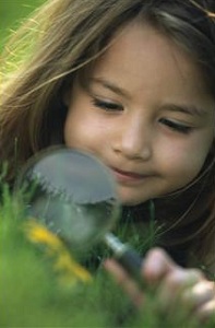 A young girl with magnifying glasslooks at things in the grass.
