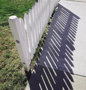 Picket fence casting shadow on sidewalk