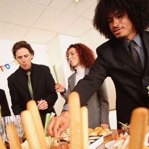 People gather around a table of food at an office party.