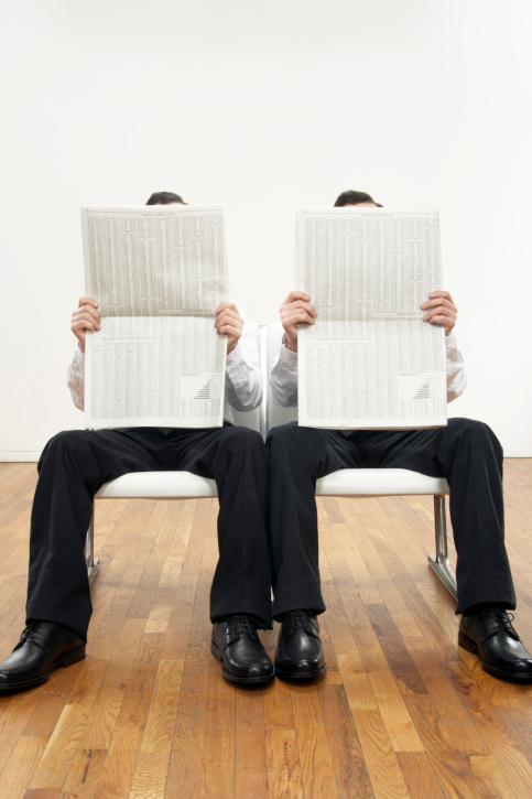 Identical twins holding newspapers to face