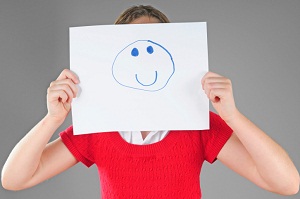 Woman holding drawn smiley face in front of face