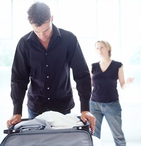 Man packing suitcase while woman talks in background