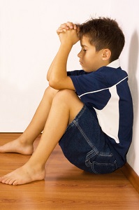 Unhappy boy sitting on floor in corner