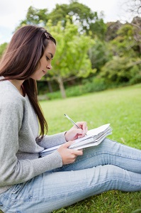 Girl sits in grass writing in a journal