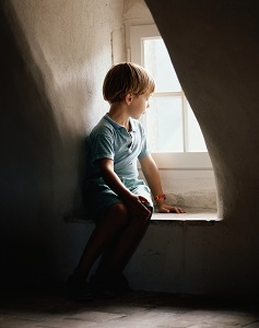 Small child looks out the window of a darkened room.