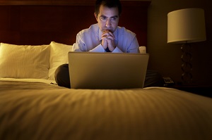 Man sitting on hotel bed with laptop