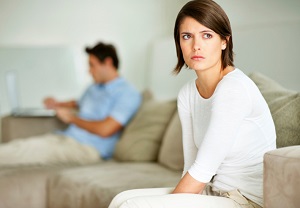 Uphappy woman sits on couch while her husband sits in background