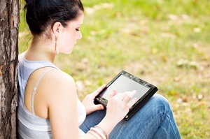 Woman with tablet leaning against tree