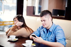 man-looks-at-smartphone-while-his-frustrated-date-waits