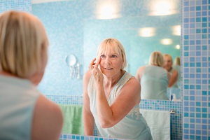 older woman applying cream to her face in mirror