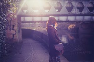 Rear view of person with long hair, head turned away, standing by canal at sunset