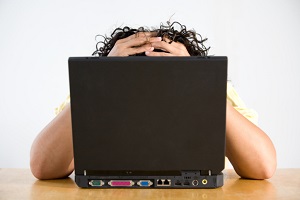 person sitting behind computer with head in hands