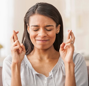 Young woman with fingers crossed at home