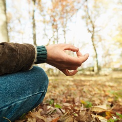 man sitting on ground meditating in rural setting.