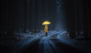 Person in yellow raincoat with yellow umbrella walks through snowy forest at night