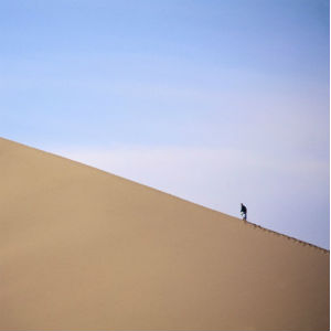 man hiking up sand dune