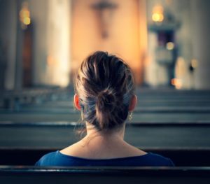 A woman sitting in a bench row in a large old christian church.