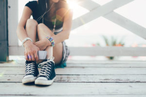 Cropped view showing shoulders-down photo of teen sitting alone on bench listening to music with phone