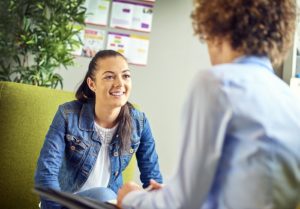 Teen woman sits in school counselor's office, chatting with the counselor