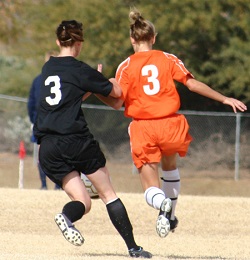 Two female soccer players from opposing teams vie for the ball