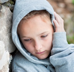 Unhappy, solitary child leans against brick wall