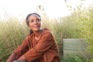 Woman with serene expression sitting in a clearing near some tall grass