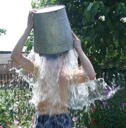 A boy dumps water from a bucket over his head