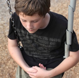 A lonely adolescent boy sits on a swing