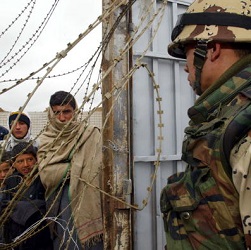 Soldier looks at civilians waiting outside a gate