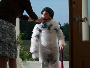 Person leaning over attaches helmet securely to child wrapped in bubble wrap