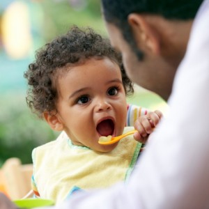 An infant eats and looks at his father