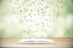 Large book lies open on wooden table and letters fly up out of it against green background