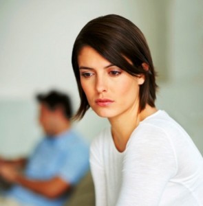 Unhappy young female sitting with her husband in the background