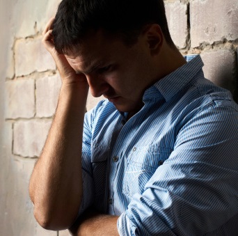A troubled man leans against a wall, looking down