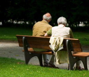 An elderly couple sits on a park bench
