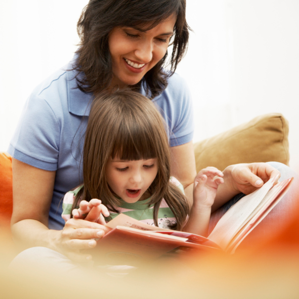 A girl reacts to a book that she is reading with her mom