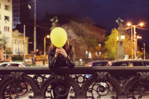 Person stands at bridge holding balloon in front of face